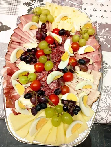 Ein großer Teller zeigt eine Auswahl an Schinken, hart gekochten Eiern, Käse, Tomaten und Trauben.