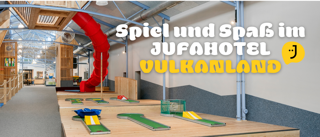 Indoor-Minigolfplatz mit mehreren Löchern. Grüne und gelbe Golfbälle liegen auf den Plätzen. Eine rote Rutsche ist im Hintergrund. Die Wände haben eine Kombination aus weißen und grauen Texturen.
