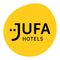 Ein gelbes kreisförmiges Logo für JUFA Hotels. Das Logo enthält den Schriftzug JUFA in stilisierter schwarzer Schrift mit einem schwarzen Punkt vor dem J. Darunter steht der Schriftzug HOTELS in normaler schwarzer Schrift.