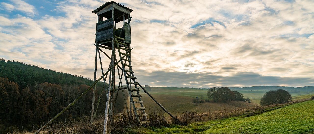 Ein alter hölzerner Aussichtsturm in einem Feld mit bewölktem Himmel.