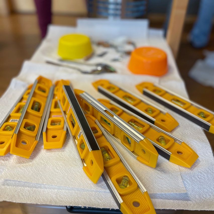 Ein mit einem weißen Tuch bedeckter Tisch zeigt mehrere gelbe Wasserwaagen mit orangefarbenen und gelben Kunststoffkappen auf dem Tisch.