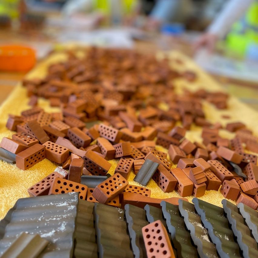 Ein Tisch mit einem gelben Tuch ist mit verschiedenen Größen und Formen von braunen Ziegelsteinen bedeckt, die möglicherweise für den Bau verwendet werden. Es gibt auch graue Ziegelsteine auf dem Tisch.