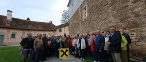 Eine Gruppe von Menschen steht vor einer Steinmauer und posiert für ein Foto. Sie tragen Winterkleidung und befinden sich in einem Park.