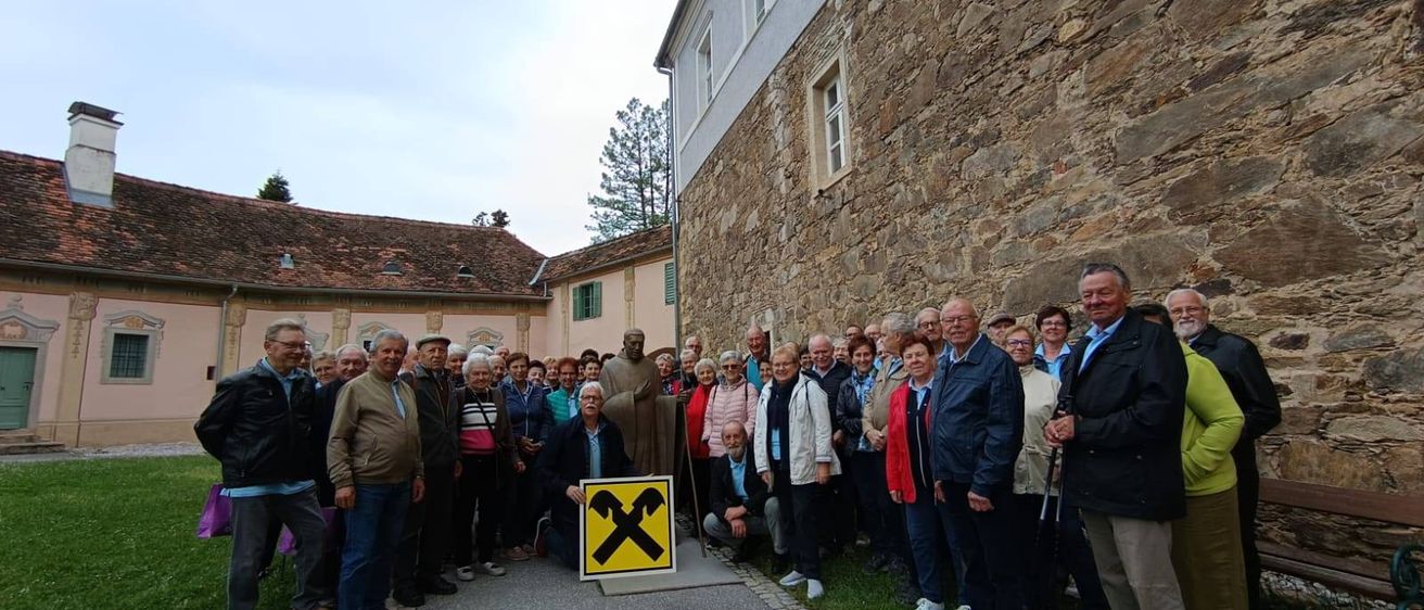 Eine Gruppe von Menschen steht vor einer Steinmauer und posiert für ein Foto. Sie tragen Winterkleidung und befinden sich in einem Park.