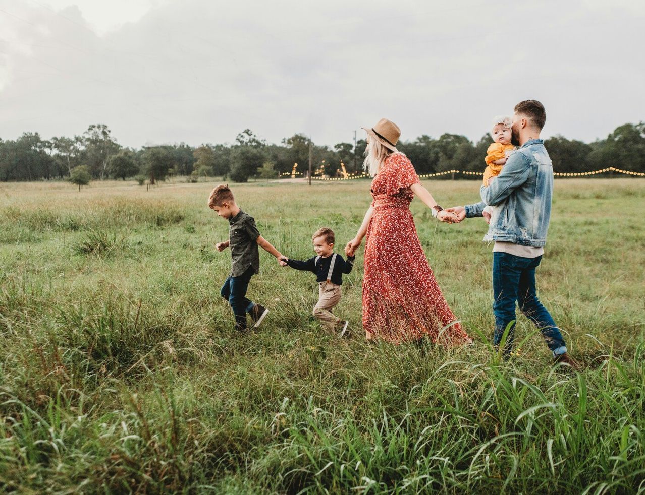 Eine vierköpfige Familie, einschließlich zwei Kindern, geht Hand in Hand auf einem Grasfeld unter einem bewölkten Himmel.