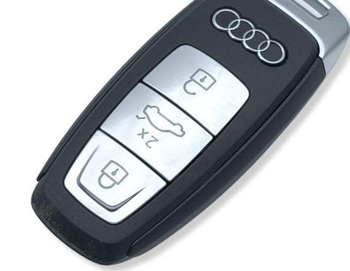 Ein schwarzer und silberner Audi-Autoschlüssel mit drei silbernen Tasten und drei silbernen Ringen mit dem Audi-Logo.
