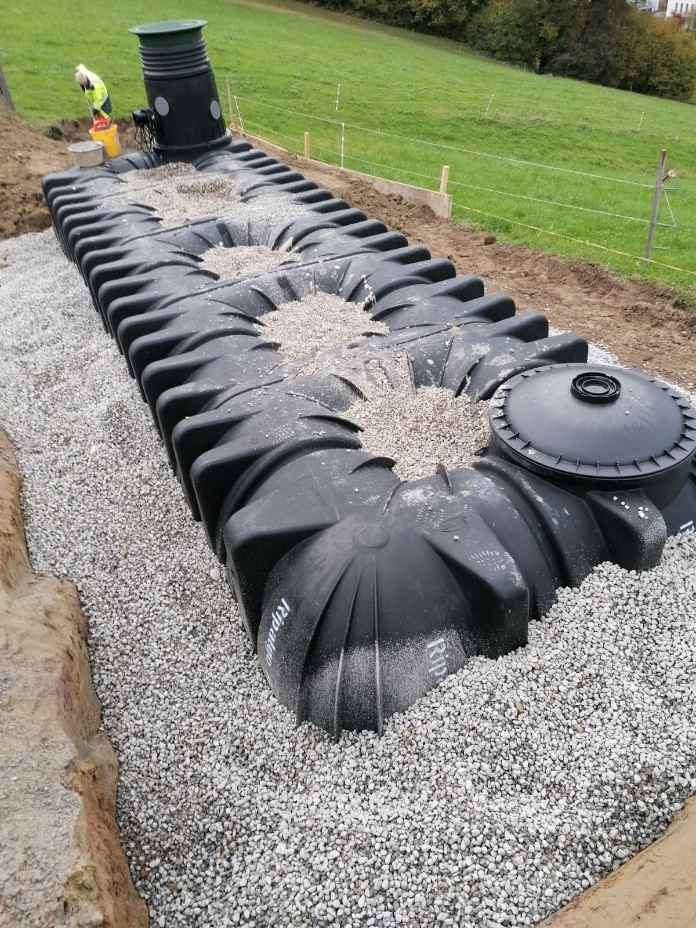 Eine Reihe großer schwarzer Kunststofftanks auf Kies mit einem offenen Oberteil ist teilweise im Boden eingegraben.