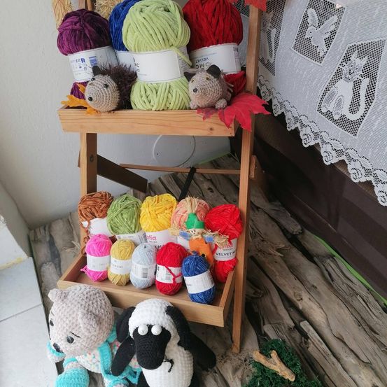 Ein Holzregal mit verschiedenen Garnknäueln und gehäkelten Tieren. Die Garne sind in verschiedenen Farben. Zwei gehäkelte Tiere sitzen auf dem Regal. Unten stehen zwei weitere gehäkelte Tiere auf dem Boden.