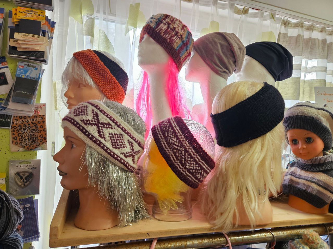 Manequins mit verschiedenen Perücken und Stirnbändern sind in einem Schaufenster ausgestellt. Jedes Mannequin hat eine andere Farbe und Stil des Stirnbandes.