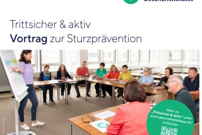 Ein Klassenzimmer mit einer Frau vor einer Tafel. Mehrere Personen sitzen an Tischen und hören einen Vortrag über Sturzprävention. Unten rechts wird eine Website angezeigt.