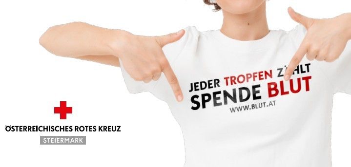 Eine Person zeigt auf ein weisses T-Shirt mit dem Text 'Jeder Tropfen Zählt SPENDEN BLUT WWW.BLUT.AT'. Darunter befindet sich ein rotes Kreuz-Symbol mit 'Oösterreichisches Rotes Kreuz' und 'Steiermark'.