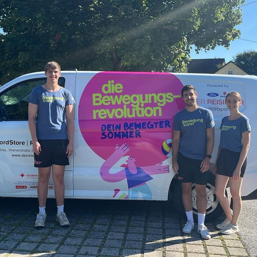 Drei Personen stehen vor einem weißen Van. Sie lächeln und scheinen für ein Foto zu posieren. Der Van hat eine pink-weiße Werbung.
