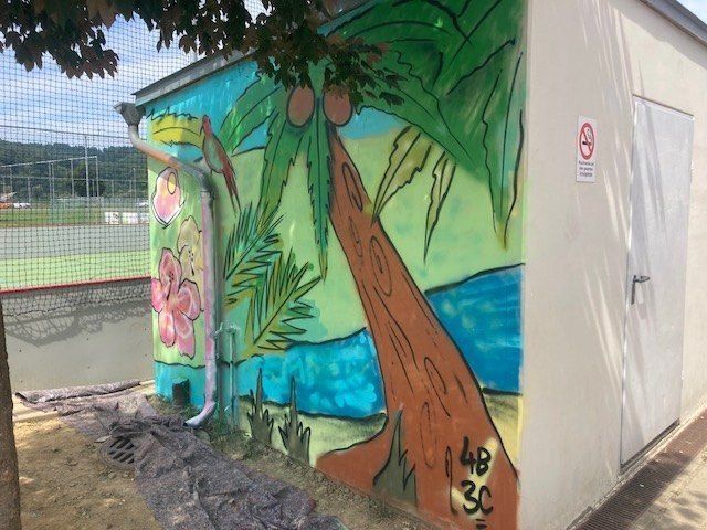 Ein Wandbild auf einem Gebäude zeigt eine tropische Szene mit einer Palme, Blumen und einem Strand. Ein 'Nichtraucher'-Schild befindet sich an der Wand.