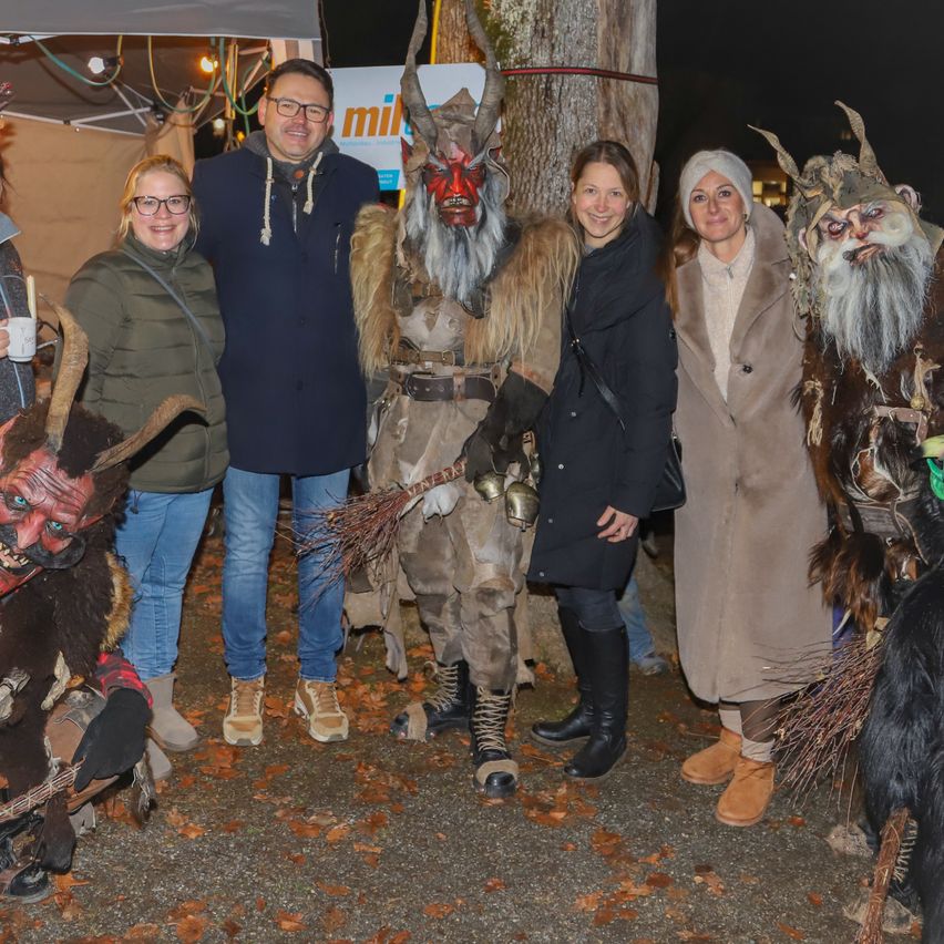 Eine Gruppe von Menschen in verschiedenen Kostümen, darunter eine Person mit einer Hörnermaske, steht nachts draußen, lächelt und posiert für ein Foto.