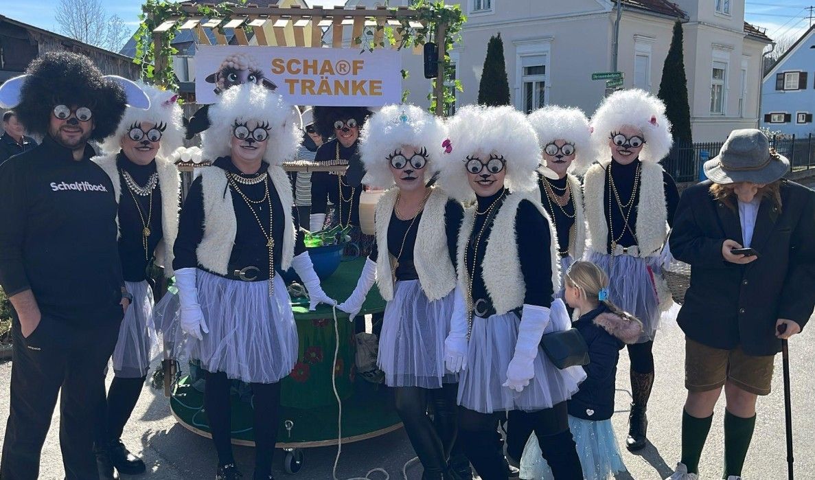 Eine Gruppe von Menschen mit weißen Perücken und Gläsern posiert für ein Foto vor einem Wagen mit einem Schild, auf dem Schaf Trunke steht.