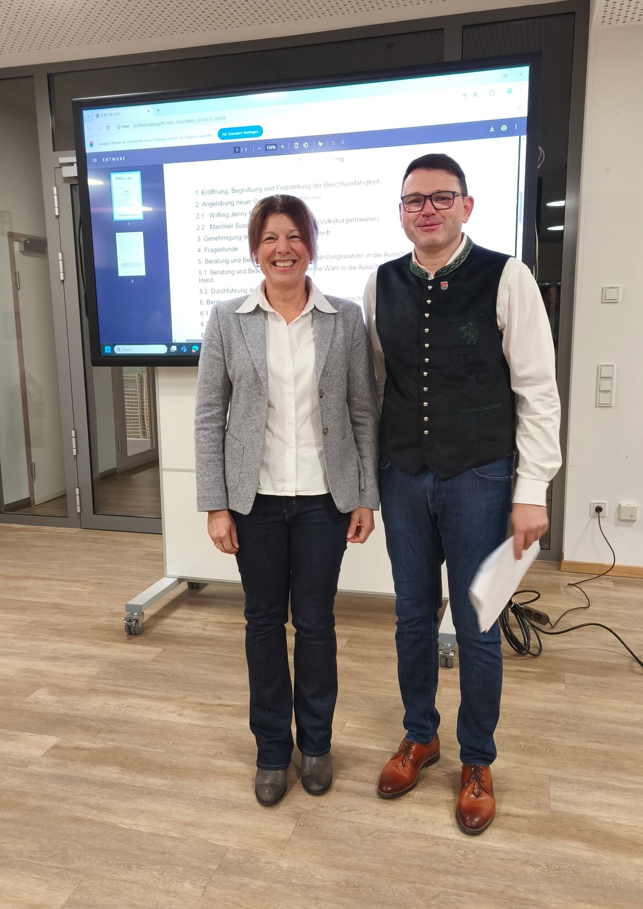 Eine Frau und ein Mann stehen eng nebeneinander vor einer großen Leinwand mit einer Liste.