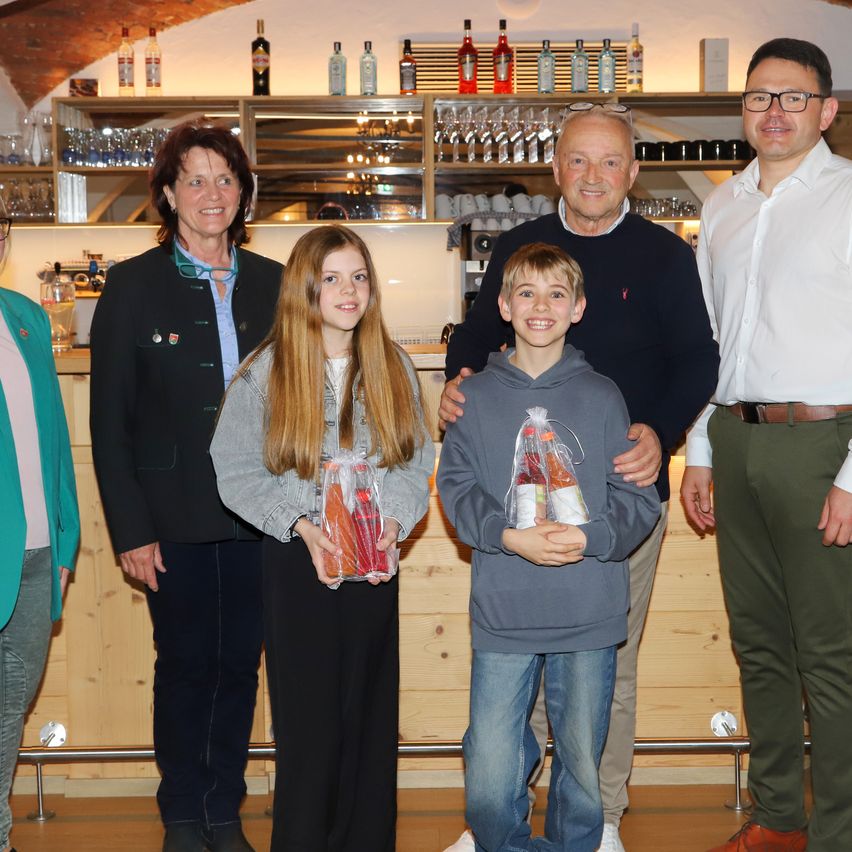 A family and two young children stand in front of a bar counter, holding plastic bags with prizes. Behind them are shelves with bottles and cups.