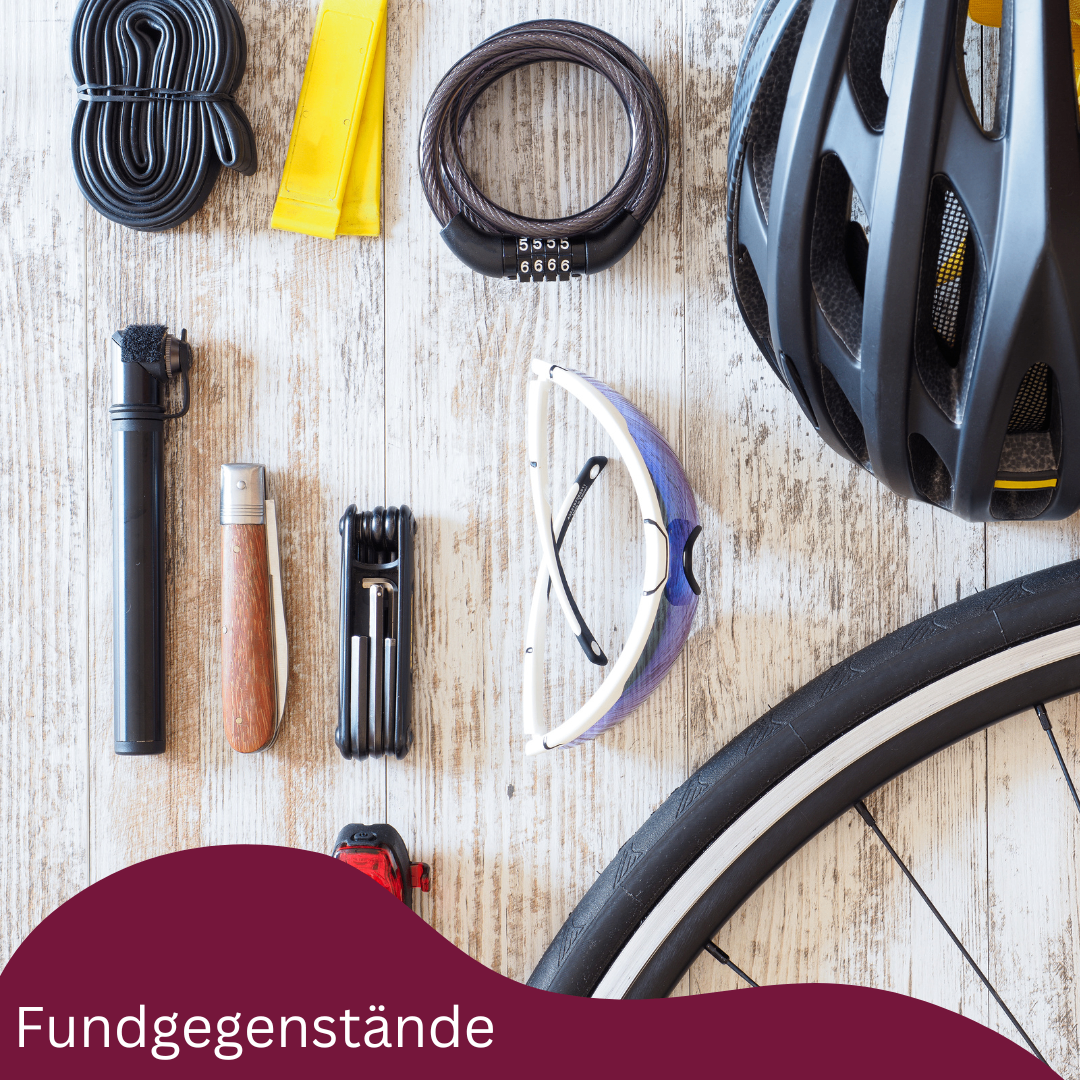 Auf einem Holztisch sind verschiedene Fahrradgegenstände wie ein Helm, eine Brille, eine Pumpe und ein Werkzeugsatz zu sehen. Das Wort 'Fundgegenstände' erscheint im Bild.