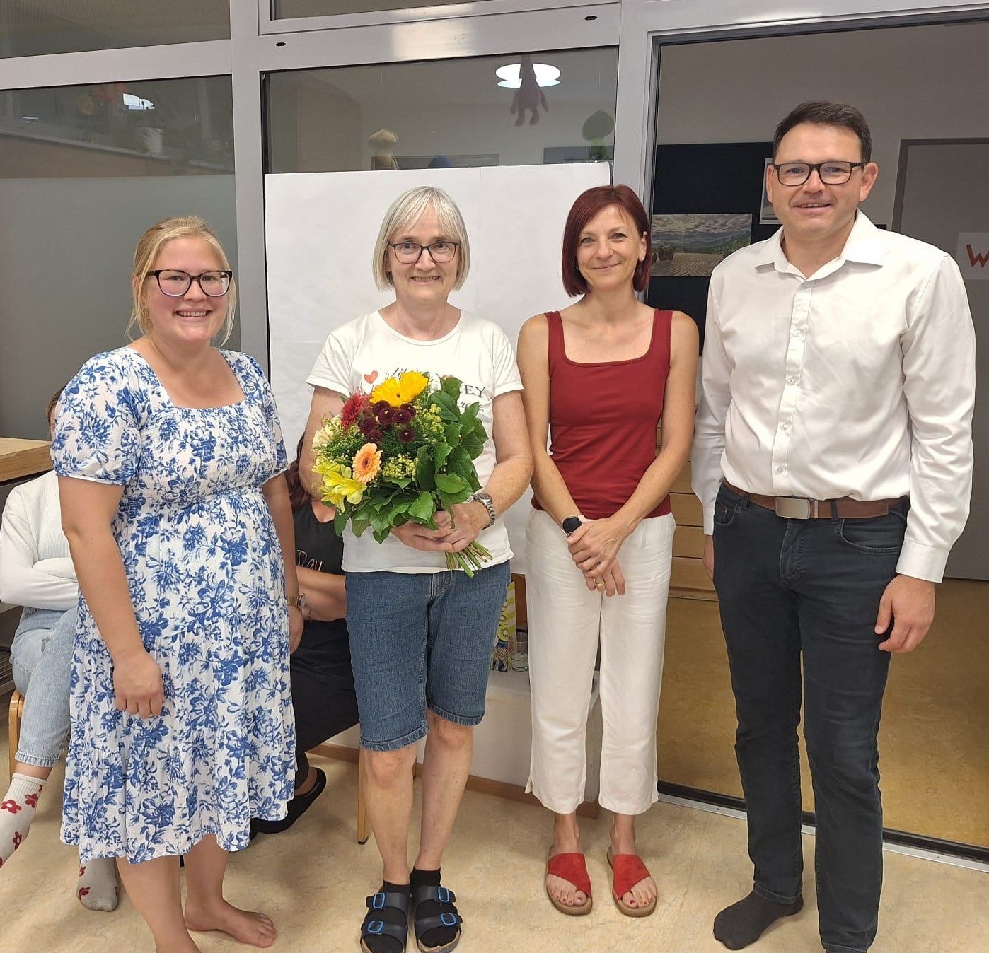 Vier Personen stehen vor einer Wand, eine Frau hält einen Blumenstrauß.