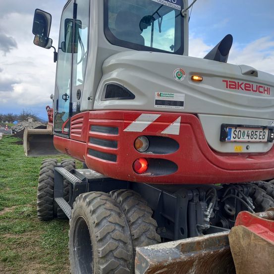 Ein roter und grauer Takeuchi-Baumaschinenfahrzeug mit einem Nummernschild steht auf einem Grasfeld.