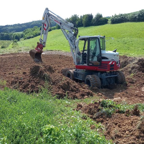 Ein roter und weißer Bagger gräbt Erde auf einem Feld aus.