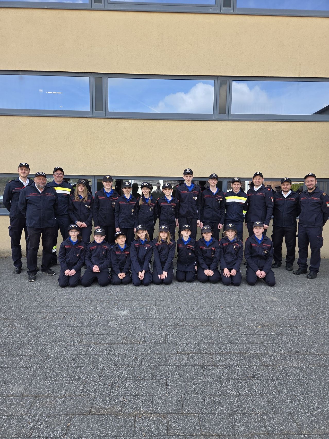 A group of people in uniform poses for a photo in front of a building with large windows.