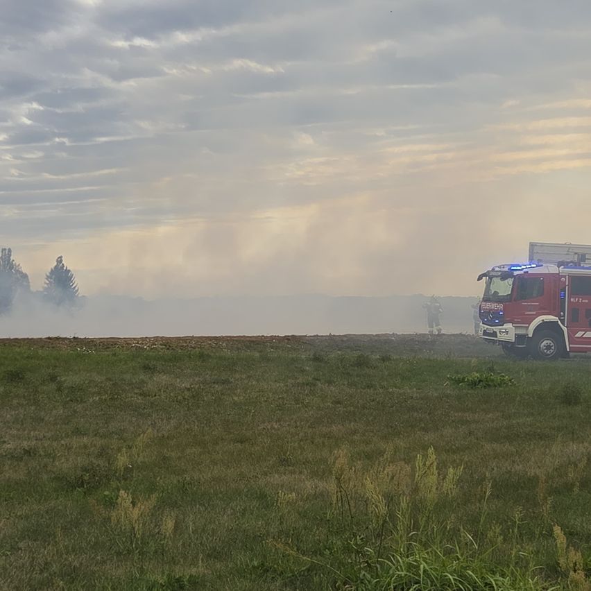A red fire truck is parked on a grassy field with smoke rising in the background.