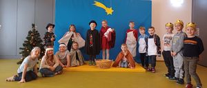 Eine Gruppe von Kindern in verschiedenen Kostümen posiert für ein Foto in einem dekorierten Raum, mit einem blauen Hintergrund, der einen Stern und einen Weihnachtsbaum im Hintergrund zeigt.