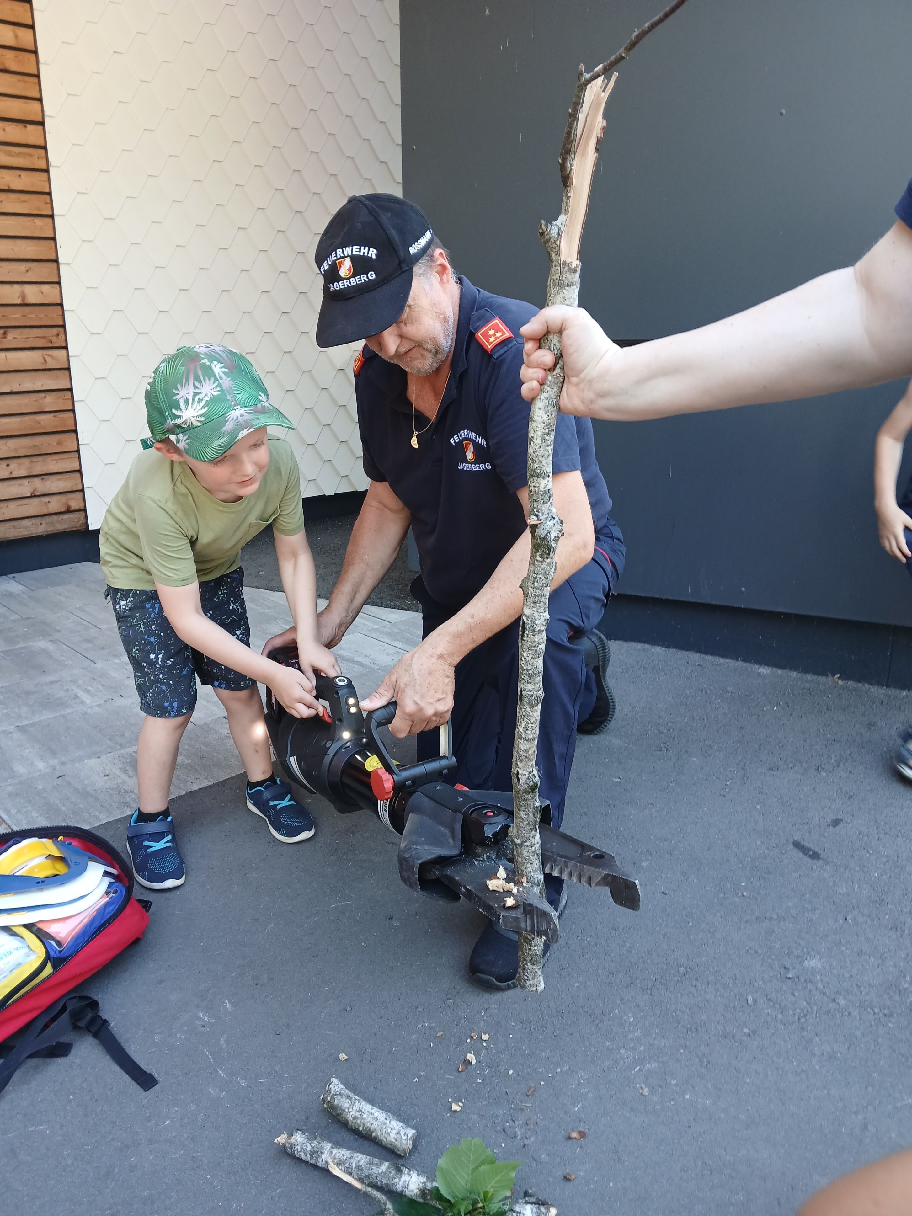 Ein Feuerwehrmann bringt einem kleinen Jungen bei, wie man eine Kettensäge an einem Ast benutzt.