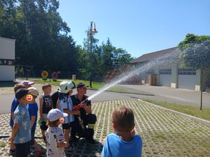 Ein Feuerwehrmann demonstriert Kindern an einem sonnigen Tag eine Feuerspritze.