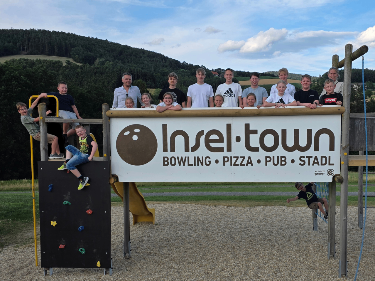 A group of people, possibly a family, pose for a photo in front of a sign for Insel Town, featuring bowling, pizza, a pub, and a stadium.