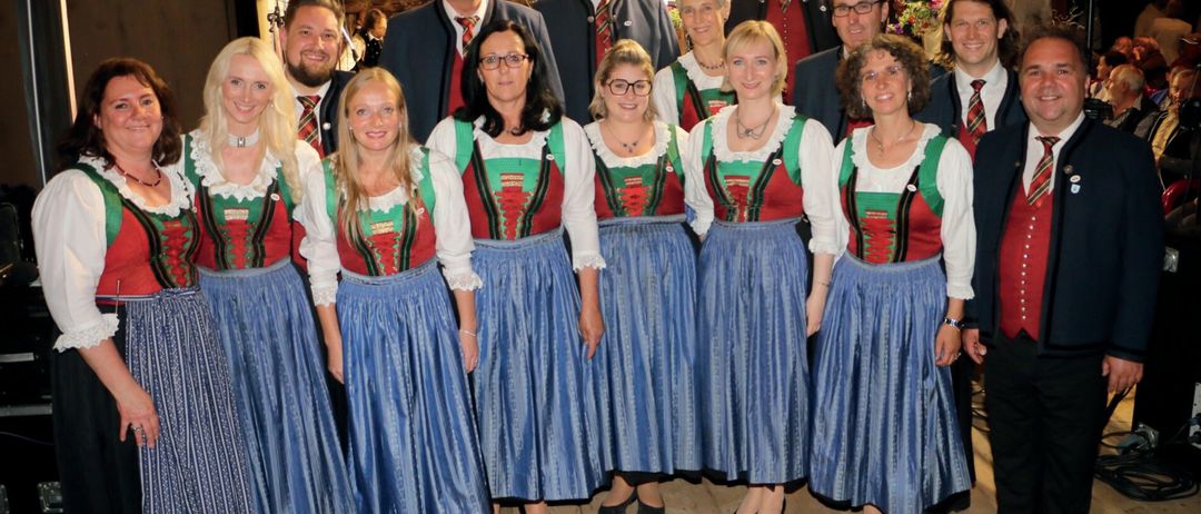 Eine Gruppe von Menschen in traditioneller deutscher Kleidung posiert für ein Foto vor einem festlichen Hintergrund, mit dem Datum 6. Dezember 2025 und dem Ort Im Gasthof.