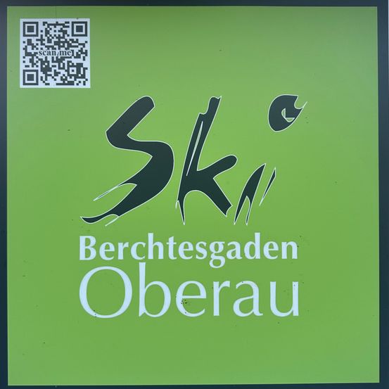 Ein grünes Poster mit 'Ski' in stilisierter Schrift und 'Berchtesgaden Oberau' darunter. Ein QR-Code befindet sich in der oberen linken Ecke.