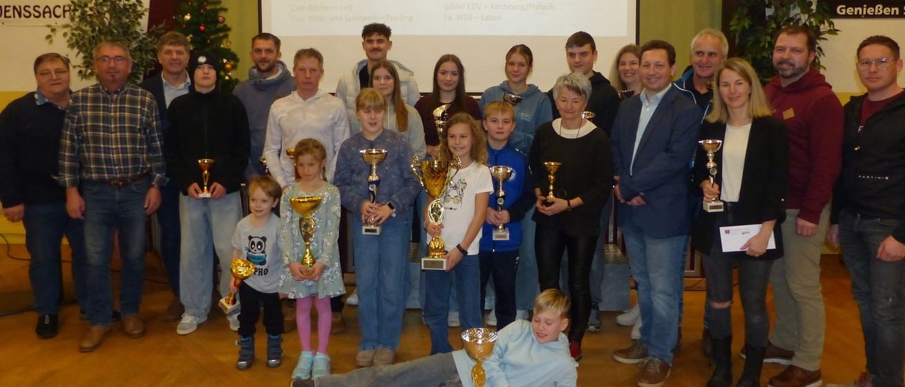 Eine Gruppe von Menschen mit Trophäen posiert für ein Foto vor einer Leinwand mit Sponsoren.