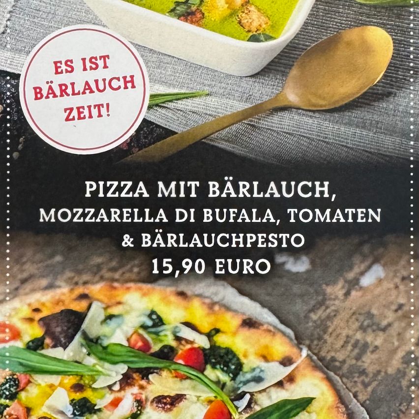 Eine Pizza mit Bärlauch, Mozzarella di Buffalo, Tomaten und Bärlauchpesto kostet 15,90 Euro. Ein Teller mit Suppe und ein Löffel sind im Hintergrund.