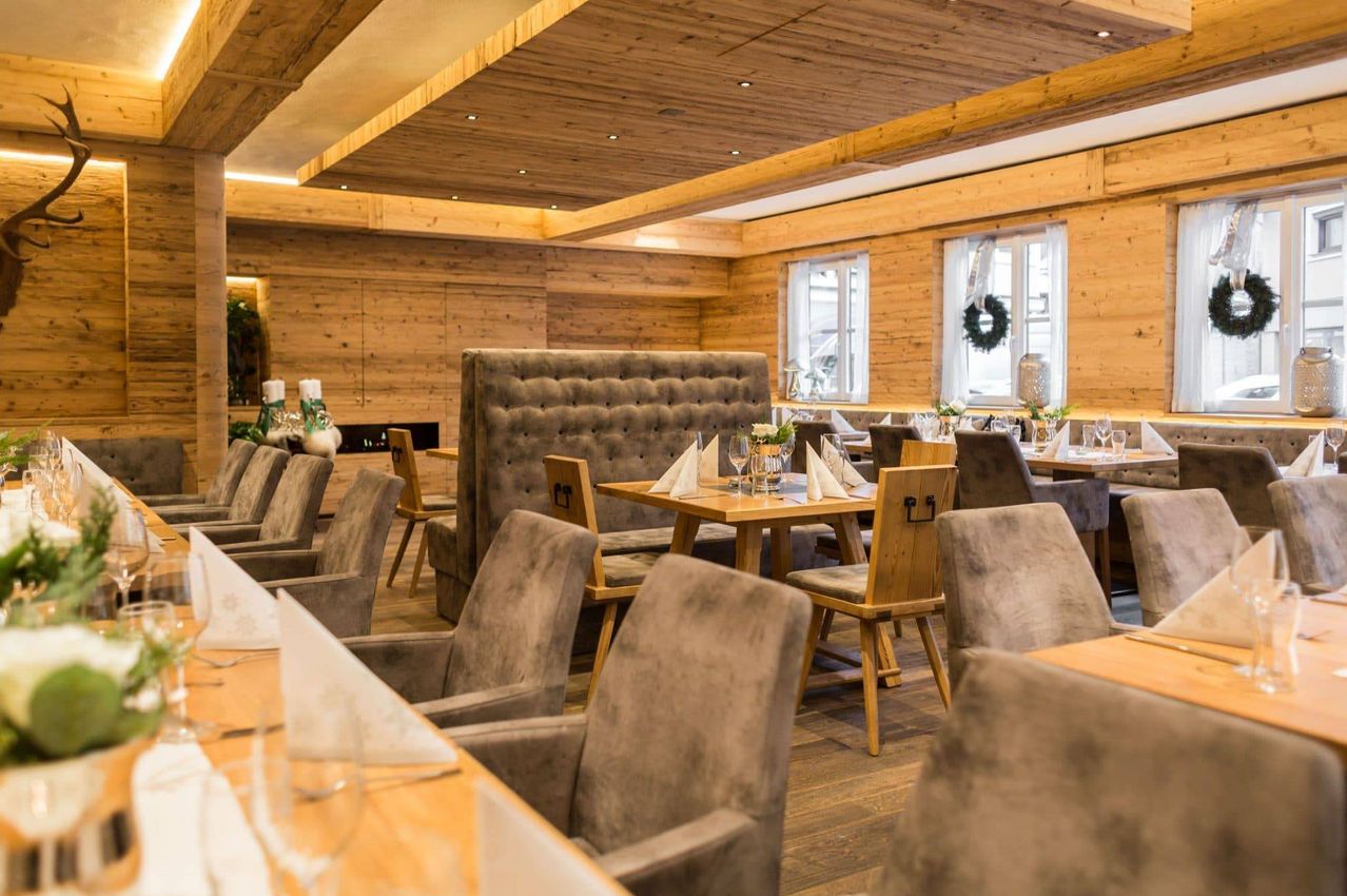 Ein leeres Restaurant mit Holzwänden, Decke und Böden. Es hat mehrere runde Tische mit Stühlen darum herum. Es gibt dekorative Gegenstände auf den Tischen.