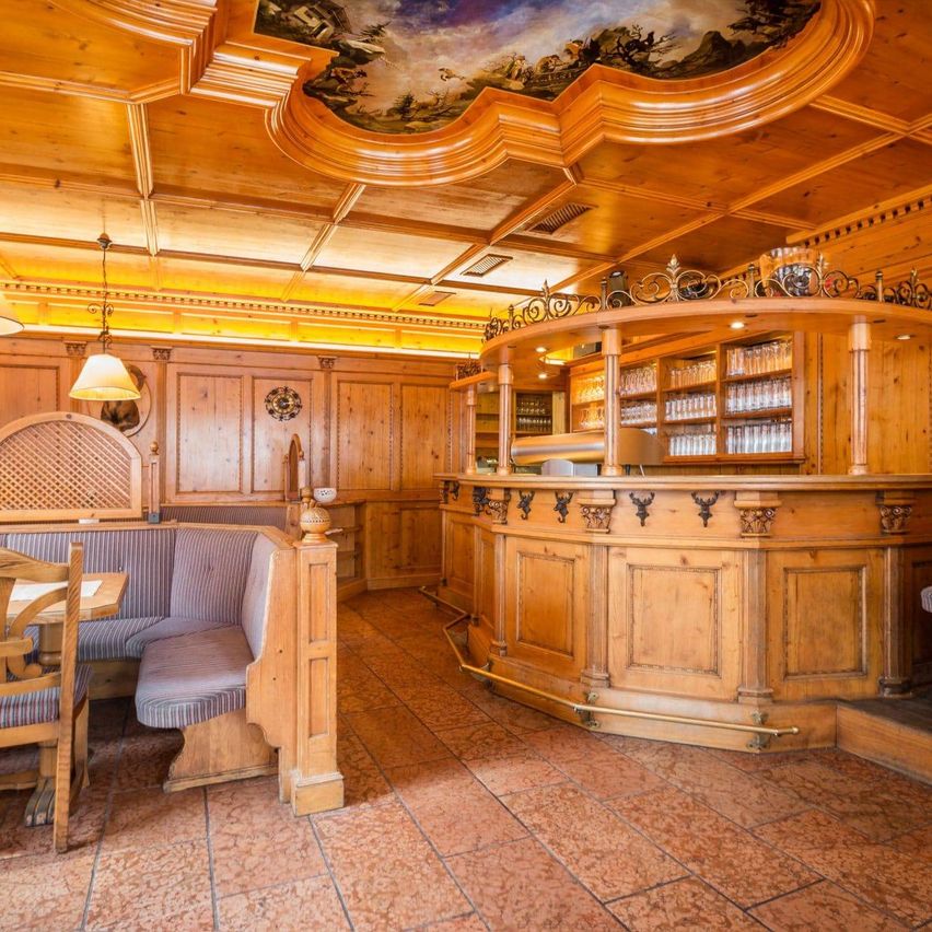 Ein eleganter Barbereich mit Holzinnenausstattung, einer dekorativen Decke und mit Gläsern gefüllten Regalen. Der Boden ist gefliest und in der Nähe befinden sich Stühle und ein Tisch.