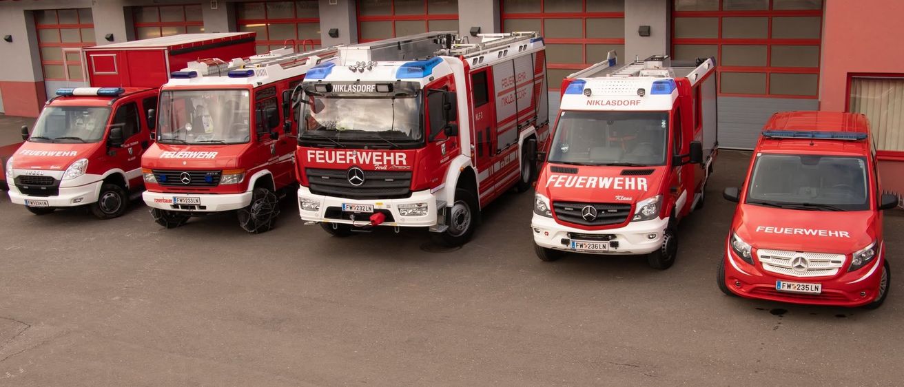 Drei rote Feuerwehrfahrzeuge sind vor einer Feuerwache geparkt. Auf der Seite jedes Fahrzeugs steht das Wort Feuerwehr geschrieben.