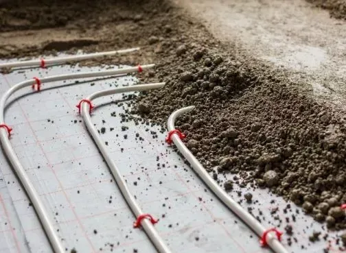 Mehrere weiße Rohre sind mit einer Schicht Erde auf einer Oberfläche verbunden, möglicherweise für ein unterirdisches Heizsystem.