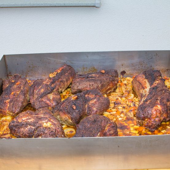 Ein Tablett mit gebratenem Fleisch und Gemüse in einem Edelstahlbehälter, vor einer weißen Wand.