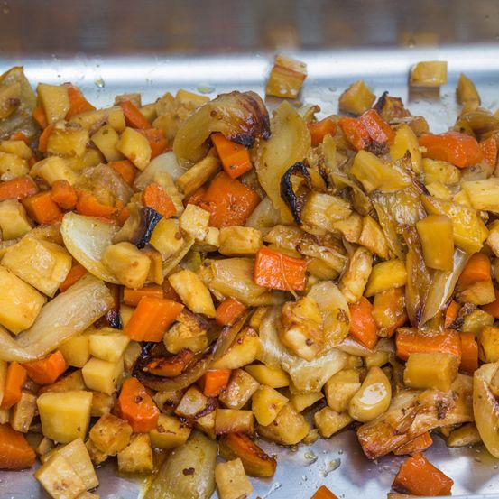 Eine Edelstahlpfanne enthält eine Mischung aus gerösteten Gemüsesorten, einschließlich Karotten, Kartoffeln und Zwiebeln, mit einigen verkohlten Rändern.