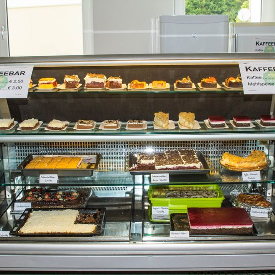 Eine Vitrine voller verschiedener Kuchen und Gebäckstücke, die mit ihren Preisen beschriftet sind, in einem Café. Die oberste Reihe hat Schokoladenkuchen, während die unterste Reihe fruchtaromatische Kuchen hat.