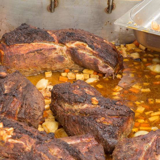 Eine Nahaufnahme von mehreren verkohlten Schweinerippchen und Fleisch in einem Topf, eingetaucht in eine reichhaltige Brühe mit gewürfeltem Gemüse.