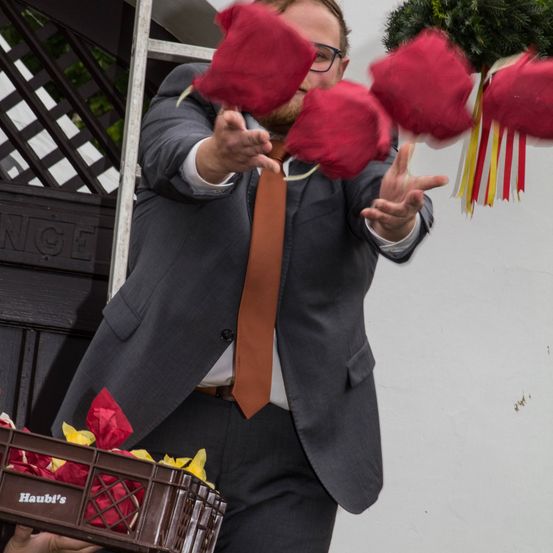 Ein Mann in Anzug und Krawatte wirft rote Blumen in die Luft im Freien.