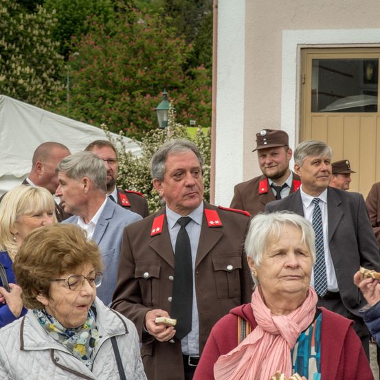 Eine Gruppe von Menschen in formeller Kleidung steht vor einem Gebäude und isst. Sie scheinen an einer formellen Veranstaltung teilzunehmen.