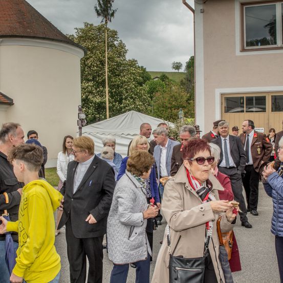Eine Versammlung von Menschen in formeller Kleidung vor einem Gebäude mit einem Zelt im Hintergrund.