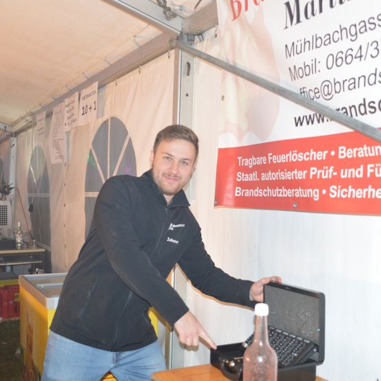 Ein Mann zeigt auf einen Laptop auf einem Tisch vor einem Banner mit Informationen über Feuerlöscher.