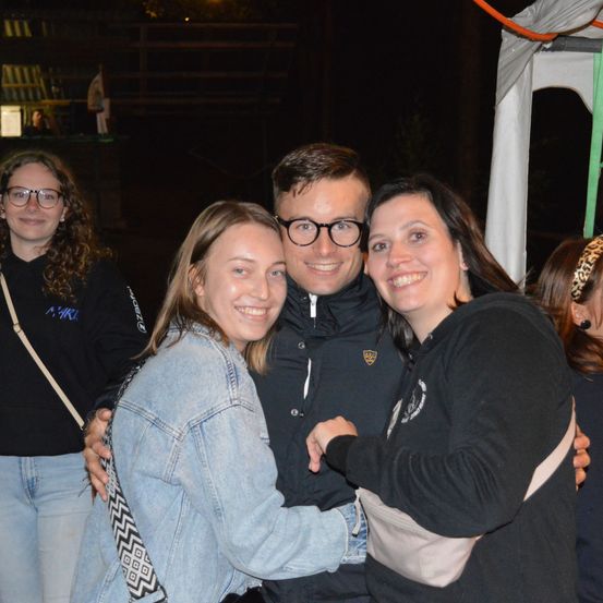 Vier Personen stehen eng beieinander und lächeln für ein Foto bei Nacht. Sie sind draußen unter einem Zelt.