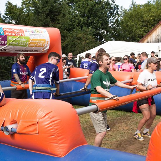 Eine Gruppe von Menschen nimmt an einer Team-Building-Aktivität mit einer aufblasbaren Hindernisstrecke teil, lächelt und lacht, während sie zusammenarbeiten.