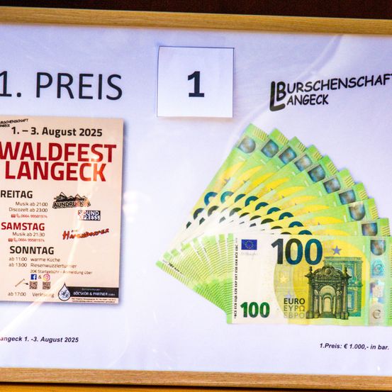 Ein gerahmtes Plakat zeigt einen 100-Euro-Schein mit einem 1. Preis-Label. Es bewirbt das Waldfest Langeck vom 1. bis 3. August 2025. Das Plakat enthält Details wie Musikzeiten, Kontaktinformationen und Sponsoren.